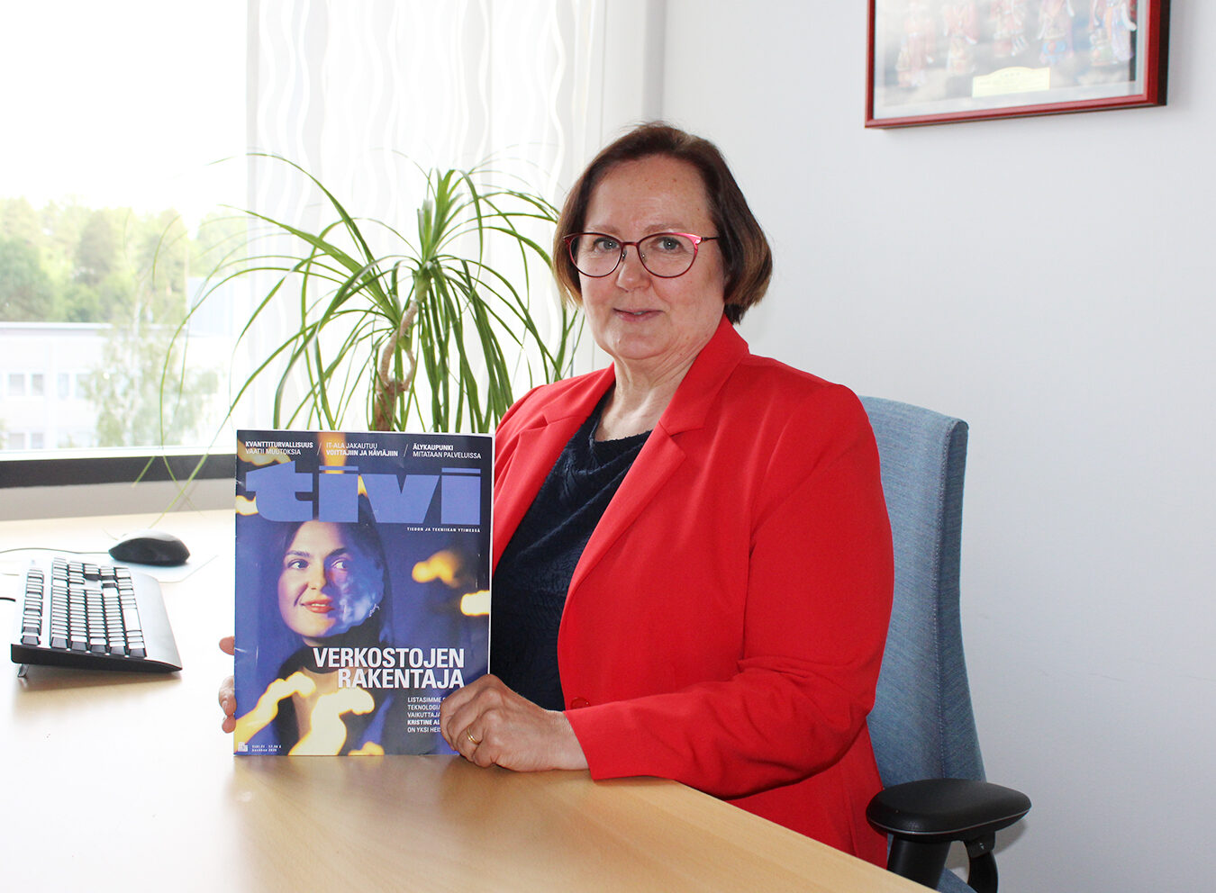 Anna-Riikka Vuorikari-Antikainen sitting by her desk, holding a TiVi magazine